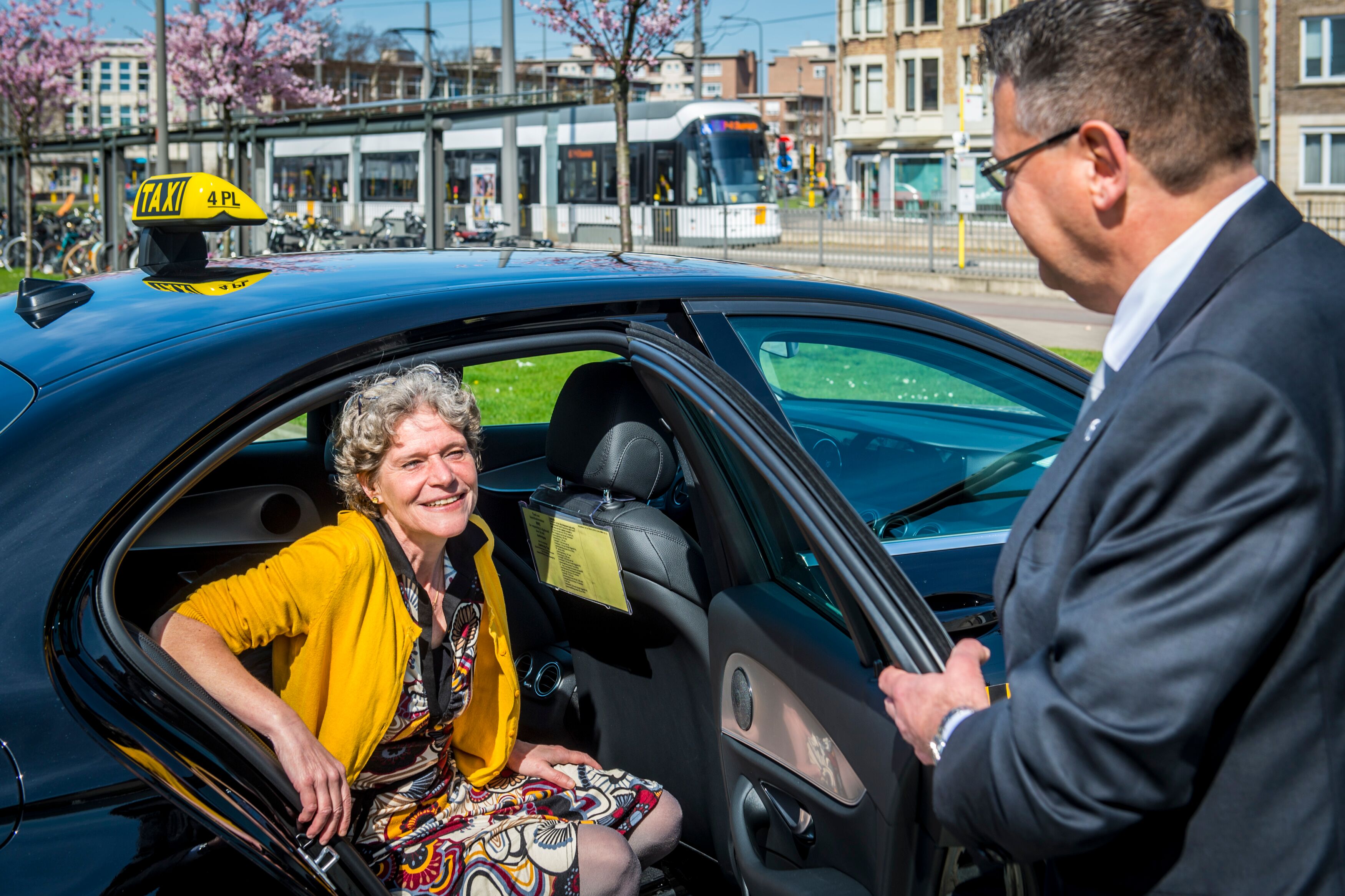 Chauffeur opent het portier voor een tevreden klant bij een zwarte taxi in een Vlaamse stad