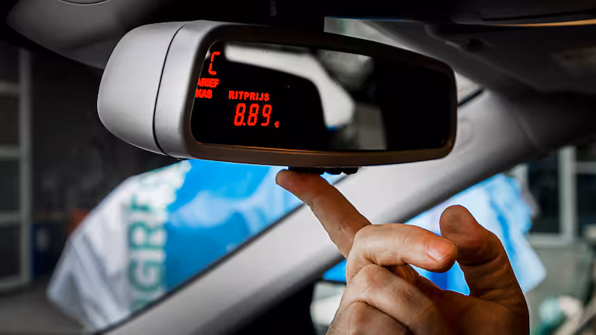 Taxameter aan de binnenspiegel die een ritprijs toont, met een hand die naar het display wijst